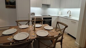 Une cuisine moderne avec des meubles blancs, une table à manger dressée pour quatre personnes et un tableau accroché au mur.