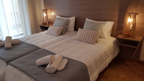 A large bed with a wooden headboard, two bedside tables with lamps, and a window with curtains. - City Center Apartment Project (Heraklion)