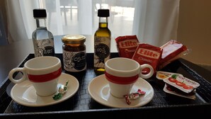 A tray with two white cups with red stripes, a bottle of olive oil, a jar of olives, and packets of Elite Classic and Mediterranean snacks. - City Center Apartment Project (Heraklion)