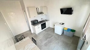 A compact kitchen with a microwave, stove, and sink. There is a small refrigerator and a TV mounted on the wall. - BeB Mezzanotte (Balvano)