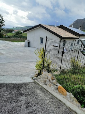 A residential property with a fenced yard, a small house with a sloped roof, and a view of the surrounding landscape. - BeB Mezzanotte (Balvano)