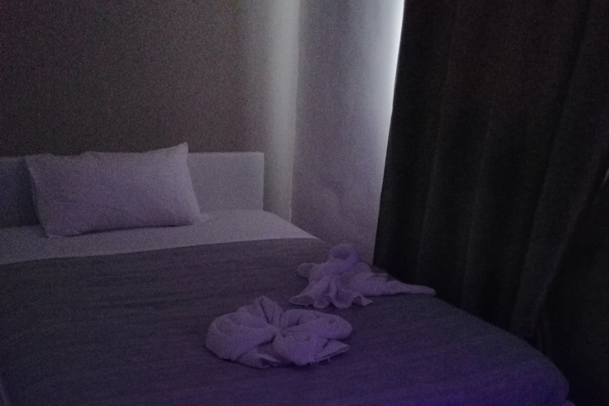 A bed with a purple blanket and a white pillow, a wooden floor, and a purple ambient light strip.