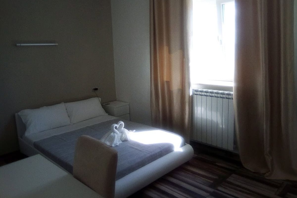 A hotel room with a bed, a bedside table, a chair, and a window with curtains.