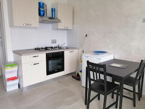 A compact kitchen with a gas stove, oven, and a small dining table with chairs. - BeB Mezzanotte (Balvano)