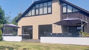 A modern house with a stone facade, large windows, and a covered patio area. - Fantastic, sociable home in the beautiful village of Brighstone, with hot tub.  (Isle of Wight)