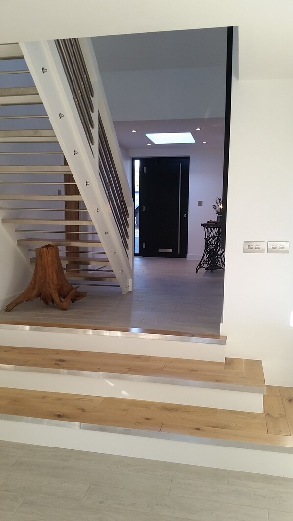 A modern staircase with a wooden tree stump at the bottom, leading to a room with a dark door and a small table with a vase.