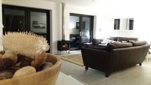 A living room with a brown sofa, a wooden bowl with rocks, a fireplace, and a sliding glass door leading to a balcony. - Fantastic, sociable home in the beautiful village of Brighstone, with hot tub.  (Isle of Wight)