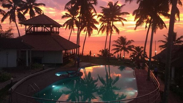 Ein Schwimmbad mit Pavillon und Palmen bei Sonnenuntergang.
