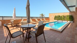A rooftop pool area with lounge chairs, umbrellas, and a small table. - PraiaBella Hotel (São Luís)