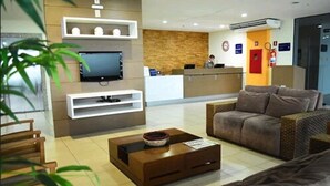A hotel reception area with a reception desk, a television, a sofa, and a coffee table. - PraiaBella Hotel (São Luís)