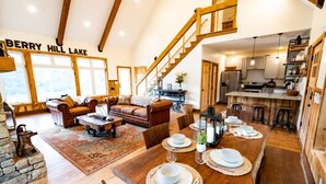 A spacious living area with a wooden staircase, a dining table set for four, and a kitchen in the background.