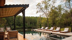A wooden deck with a pool, lounge chairs, and a pergola.