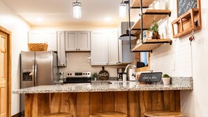 A kitchen with white cabinets, a granite countertop, wooden stools, and a chalkboard sign.