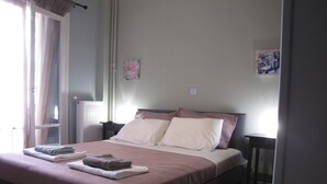 Ein ordentlich bezogenes Bett mit Kissen und gefalteten Handtüchern, ein Nachttisch und ein Fenster mit Vorhängen.