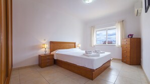 Une chambre à coucher avec un lit en bois, des tables de chevet, une commode et une fenêtre avec des rideaux.