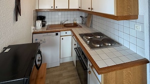 A compact kitchen with white cabinets, a stove, a dishwasher, and a coffee maker. - Seignosse Ocean, apartment rated 2 stars, right next to Penon beach (SEIGNOSSE)