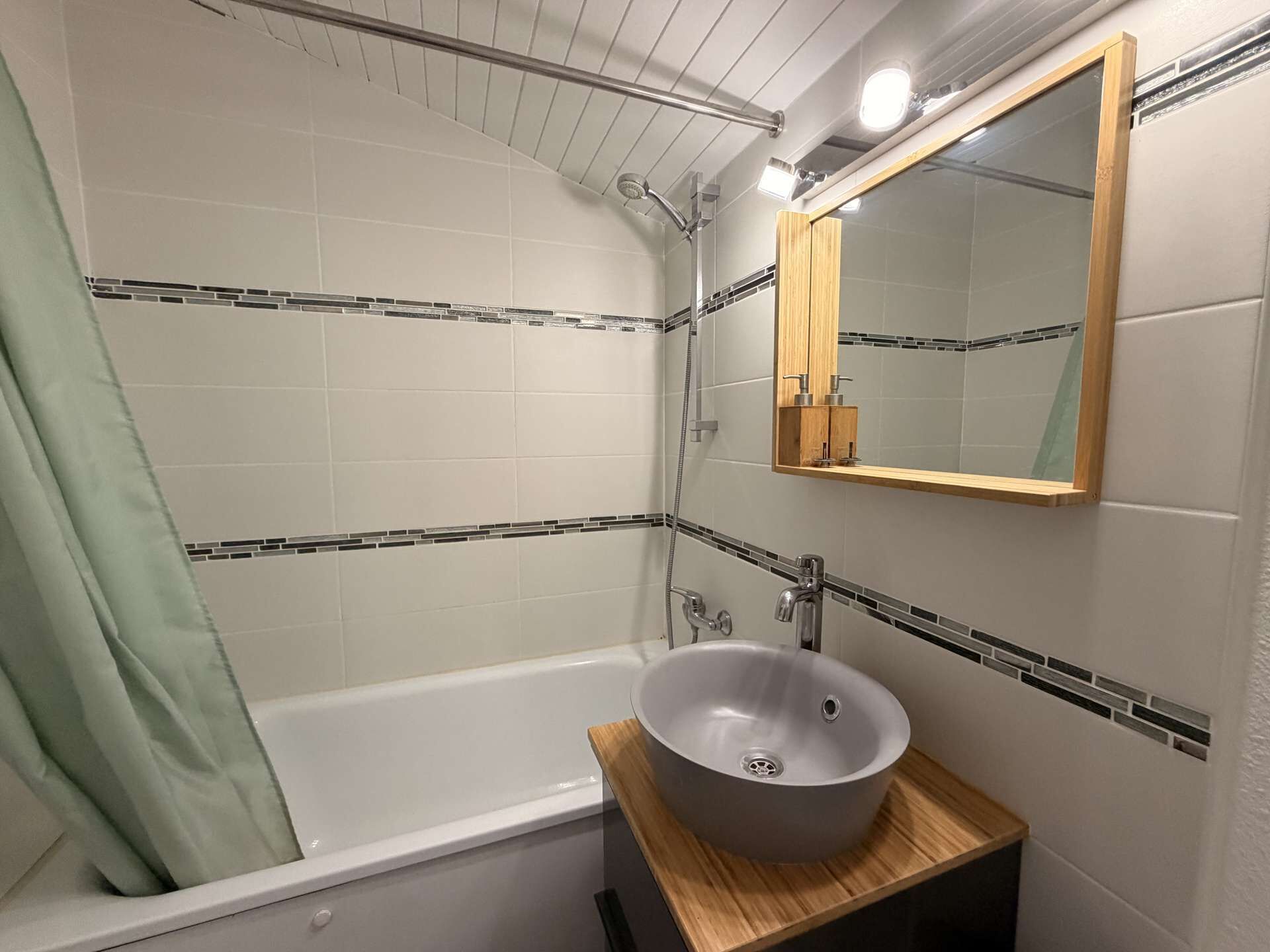 Ett badrum med badkar, handfat med en fristående skål, dusch och en spegel med träram.
