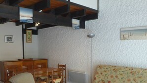 A living room with a wooden dining table, chairs, a sofa, and a small white table.