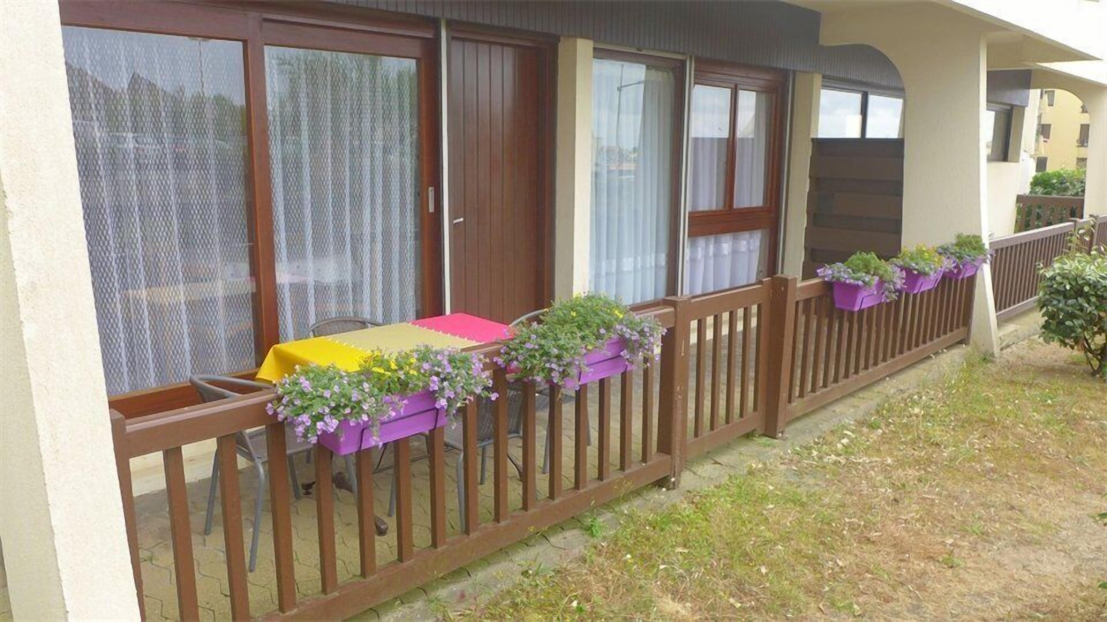 A balcony with a table and chairs, a wooden fence, and potted plants.
