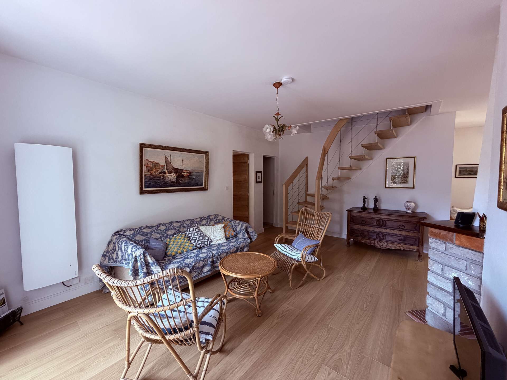 A living room with a sofa, two wicker chairs, a small round table, and a staircase leading to another level.
