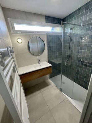 Une salle de bain moderne avec une douche à parois de verre, un lavabo blanc avec un meuble-vasque en bois et un miroir rond.