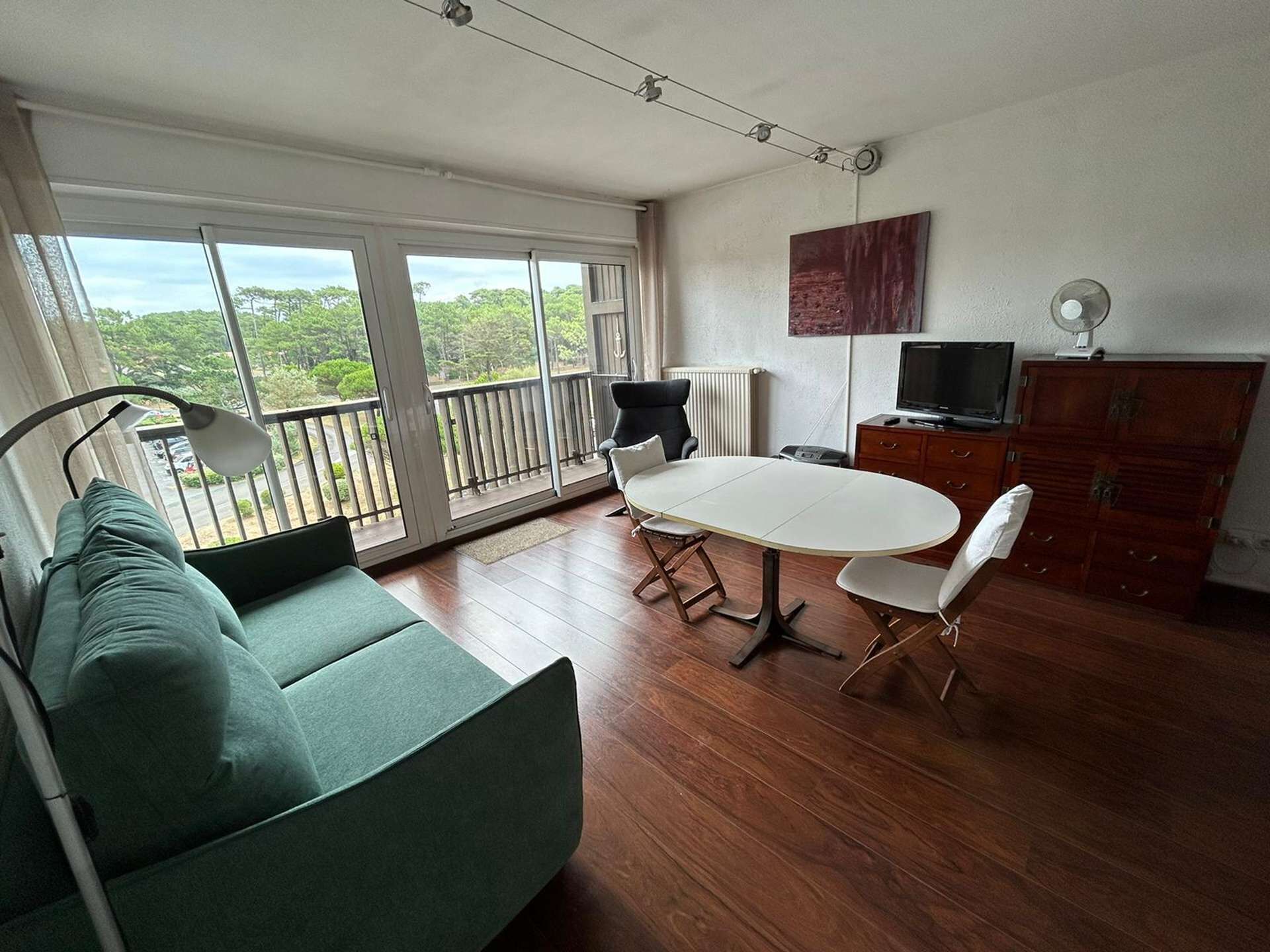 A spacious room with a green sofa, a dining table with chairs, a TV, and a wooden cabinet.