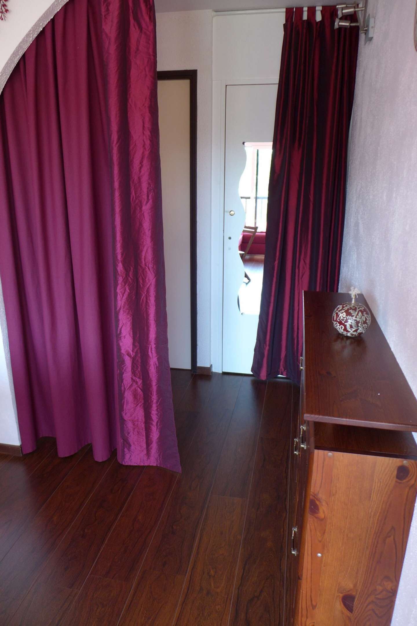 Een kamer met een houten vloer, een houten kast en een deur met een rood gordijn.