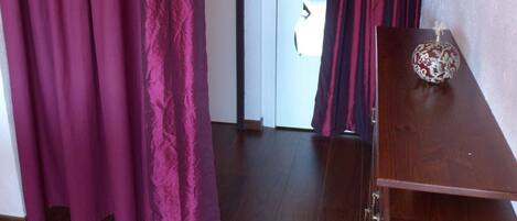 Een kamer met een houten vloer, een houten kast en een deur met een rood gordijn.