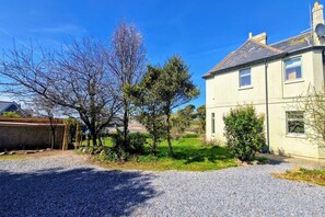 A residential property with a gravel driveway, a house with a pitched roof, and a clear blue sky.