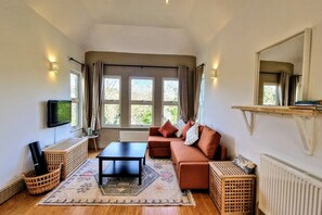 A living room with a sofa, a coffee table, a TV, and large windows.