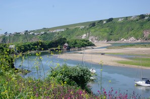 A coastal landscape with a river, boats, and houses on a hillside.