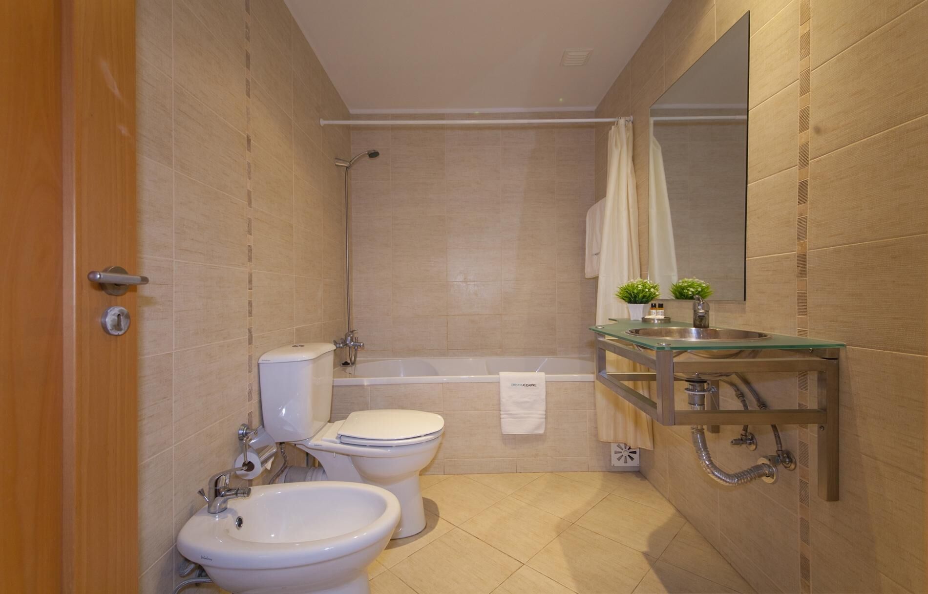 Un baño con inodoro, bidé, bañera y un lavabo con espejo, envuelto en vidrio.