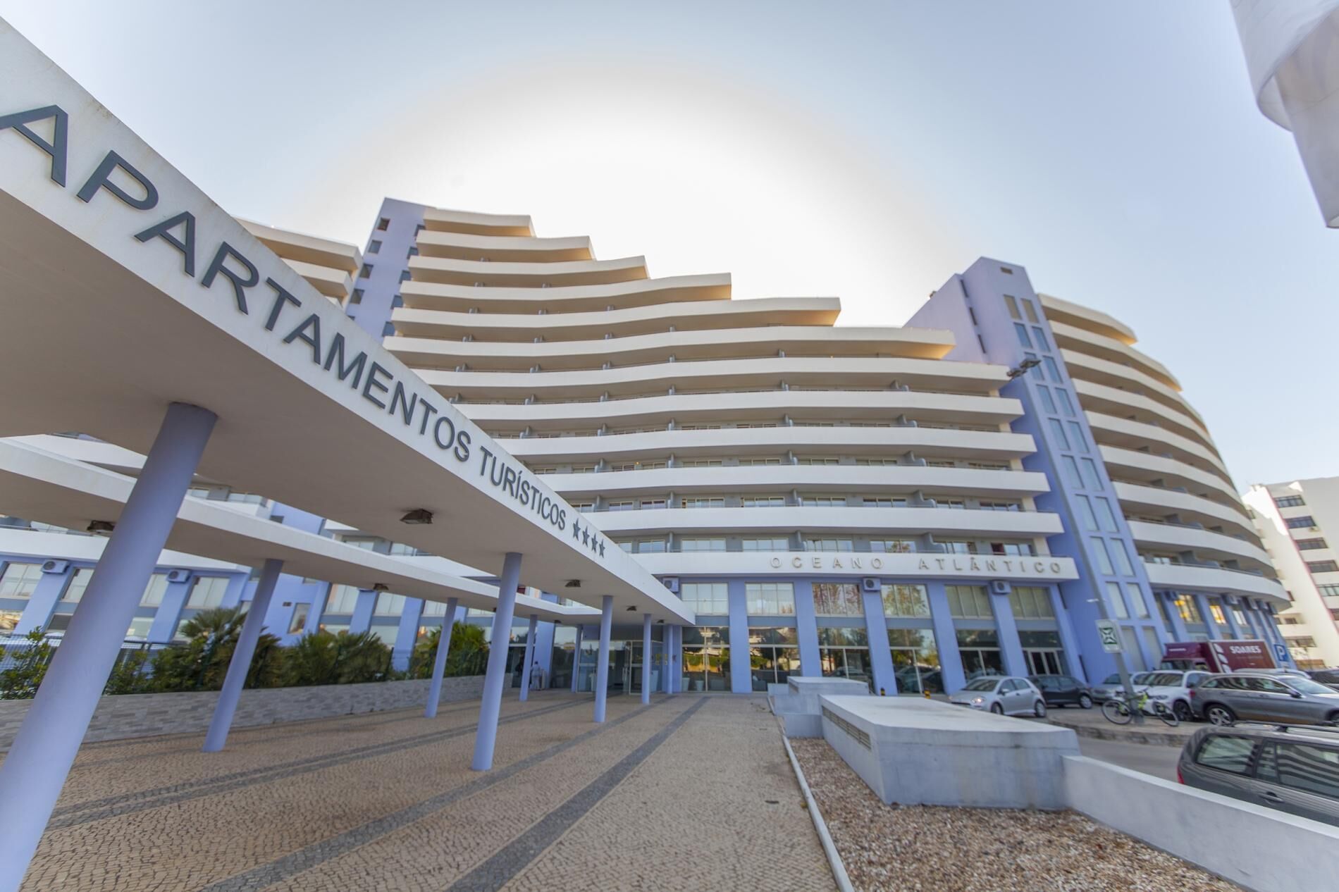 Een modern hotel met een gebogen gevel, meerdere balkons en een opvallend bord dat het een toeristenaccommodatie aangeeft.
