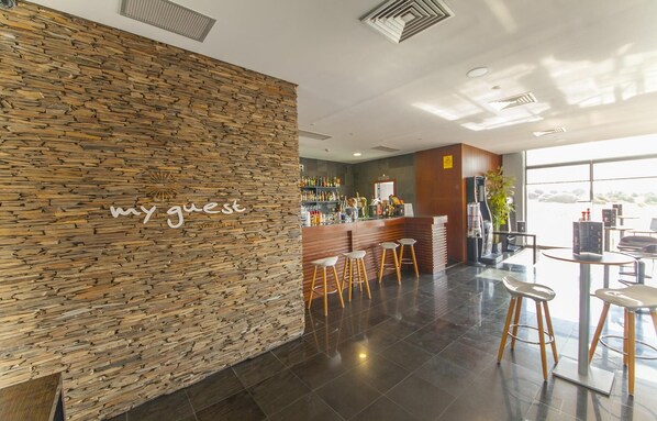 Un espace bar moderne avec un mur en pierre, des tabourets de bar et un comptoir bien garni.