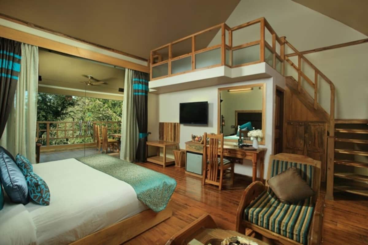 Une chambre spacieuse avec un grand lit, un balcon, un escalier en bois et un coin bureau.