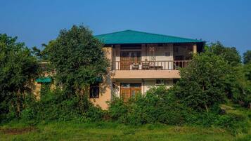 A two-story building with a green roof, surrounded by lush greenery.