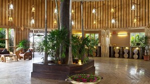 Eine großzügige Lobby mit Holzvertäfelung, großen Fenstern und einem zentralen Pflanzgefäß mit tropischen Pflanzen.