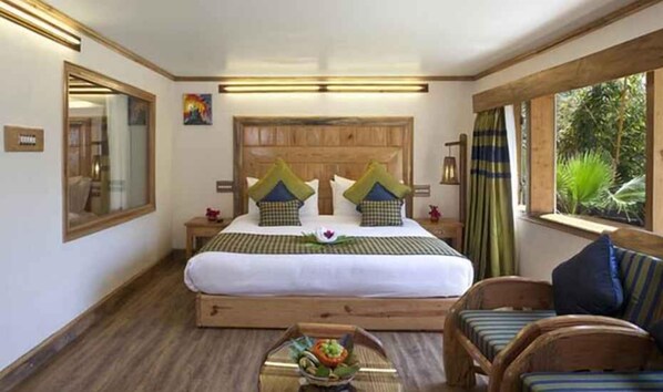 A bedroom with a wooden bed frame, a large mirror, a bedside table, a chair, and a window with curtains. - The Rangers reserve Jim Corbett (Nainital)