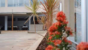 A modern building with a covered outdoor area, a concrete patio, and a row of palm trees. - Pousada Santana (Trindade)