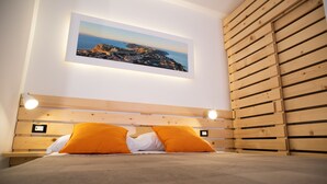 Une chambre à coucher avec une tête de lit en bois, un tableau représentant un paysage encadré et deux coussins orange.