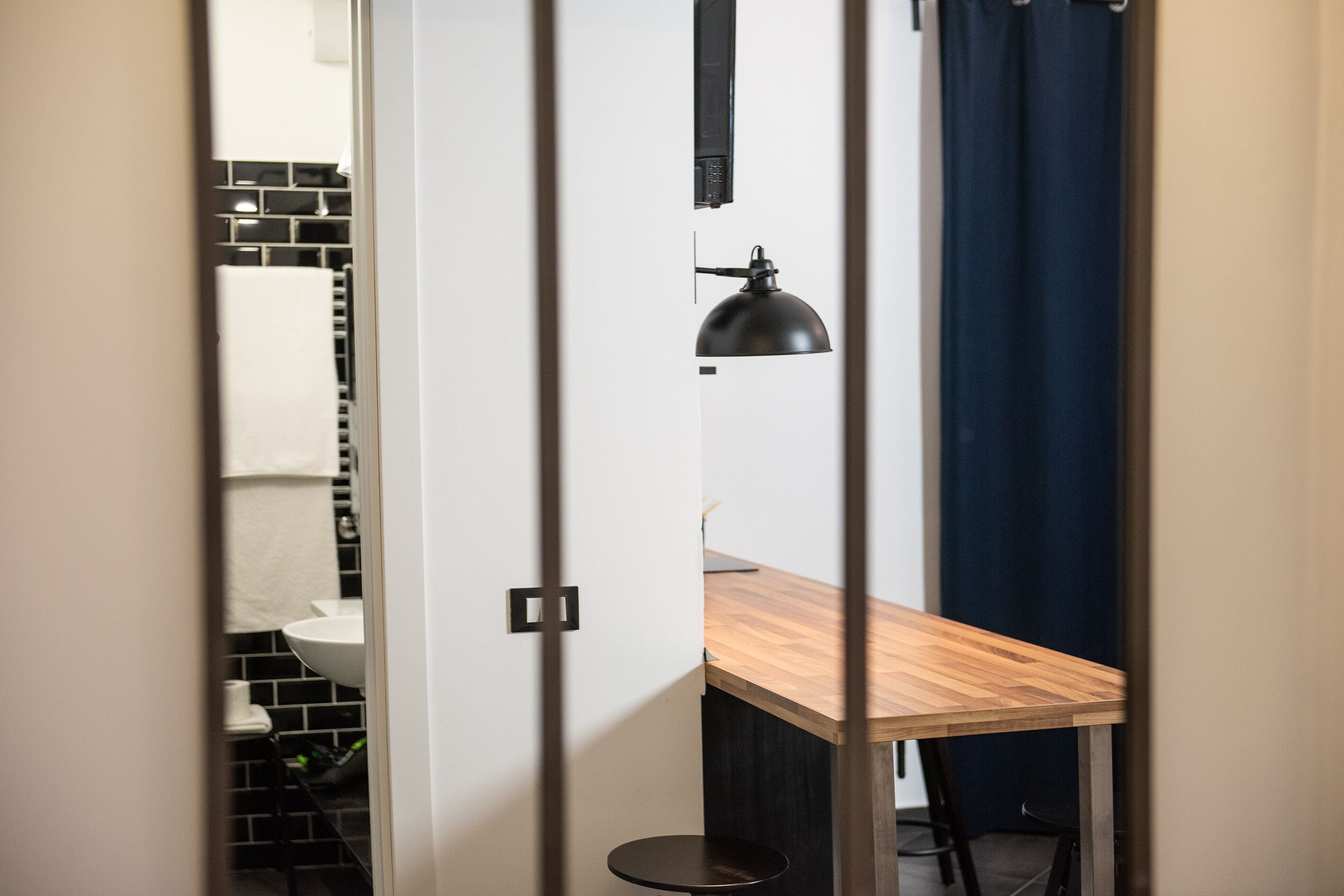 Un baño moderno con un salpicadero de azulejos blanco y negro, un lavamanos blanco y una lámpara de pie negra.