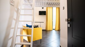 Un intérieur moderne avec une échelle blanche, une chaise jaune, un téléviseur à écran plat et un coin cuisine agrémenté de rideaux jaunes.