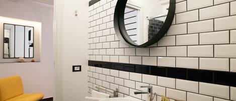 A bathroom with a white sink, black-tiled walls, a round mirror, and a yellow chair.