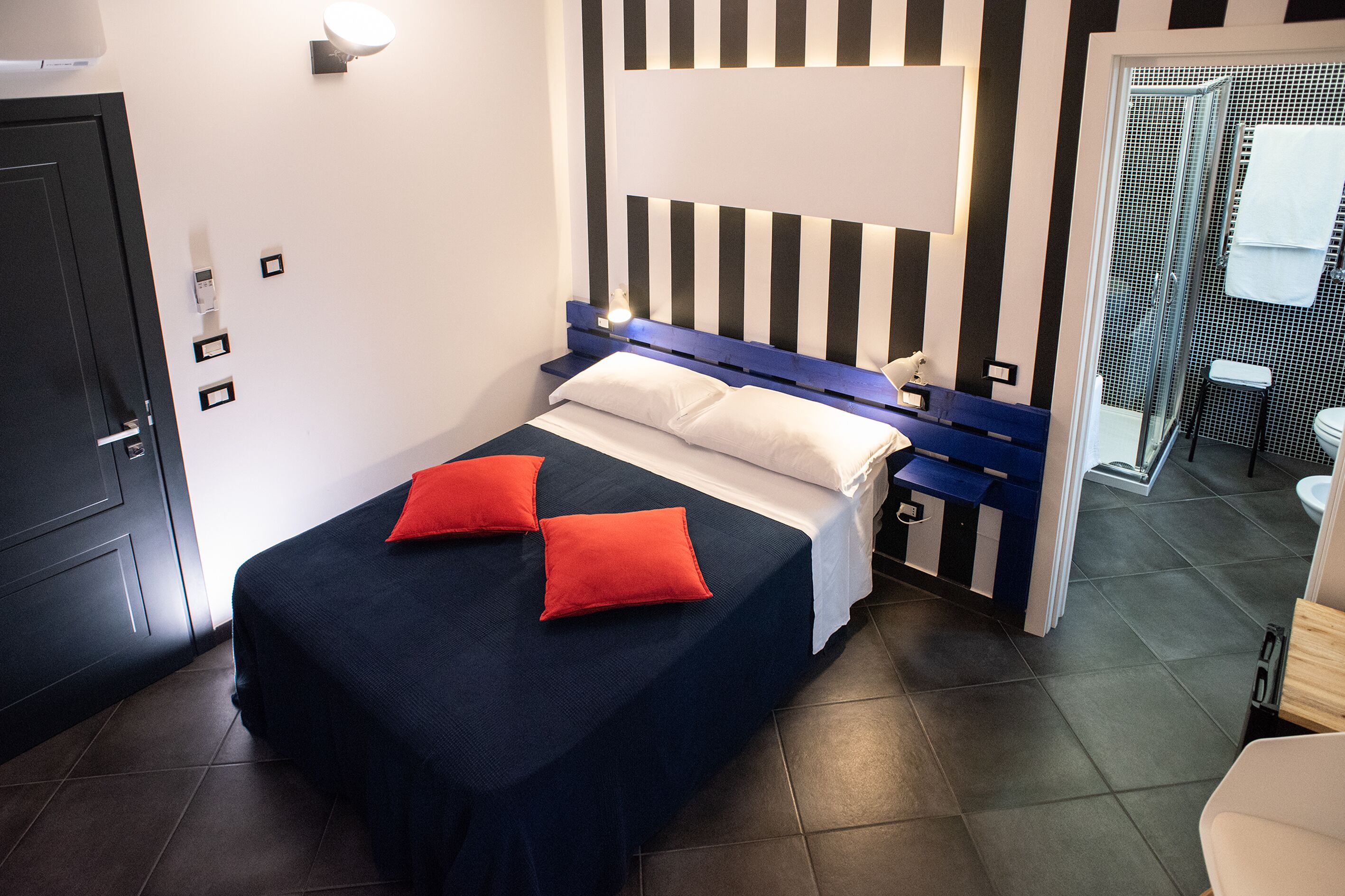 Una habitación de hotel con cama, mesita de noche, baño con ducha y puerta.