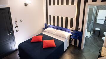 Una habitación de hotel con cama, mesita de noche, baño con ducha y puerta.