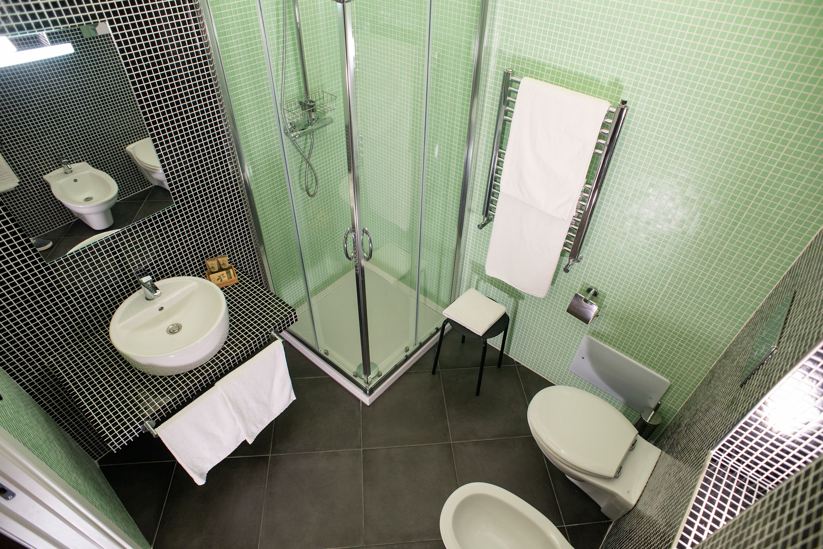 A bathroom with a glass-enclosed shower, a sink, a toilet, and a small stool.