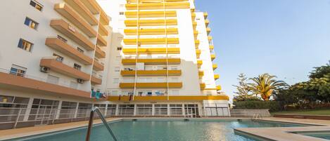 Un hotel de varios pisos con balcones, piscina y cielo despejado.