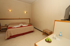 A hotel room with a bed, bedside table, a small table with a bowl of fruit, a water bottle, and a television. - Hotel Ferri (Oaxaca)