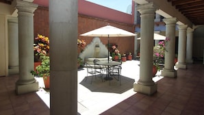 Un patio exterior con una mesa y sillas, rodeado de columnas y plantas en macetas.