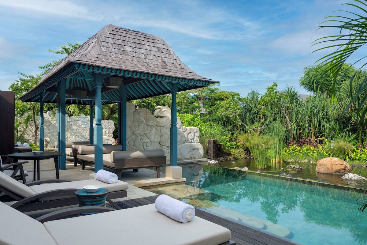 A poolside area with lounge chairs, a gazebo, and a stone wall.